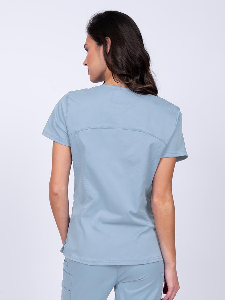 Young female nurse wearing an Epic by MedWorks Women's Knit Collar Mock Wrap Scrub Top in blue fog with stylish seaming throughout.