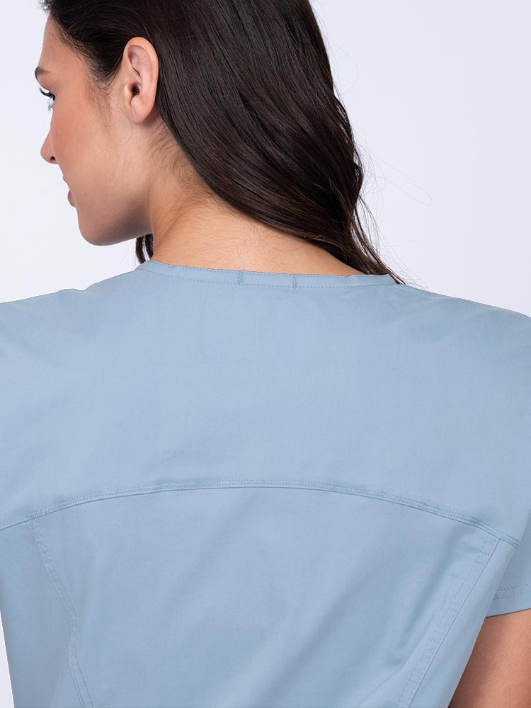 Young woman wearing an Epic by MedWorks Women's Knit Collar Mock Wrap Scrub Top in blue fog with a back yoke to ensure a flattering fit.