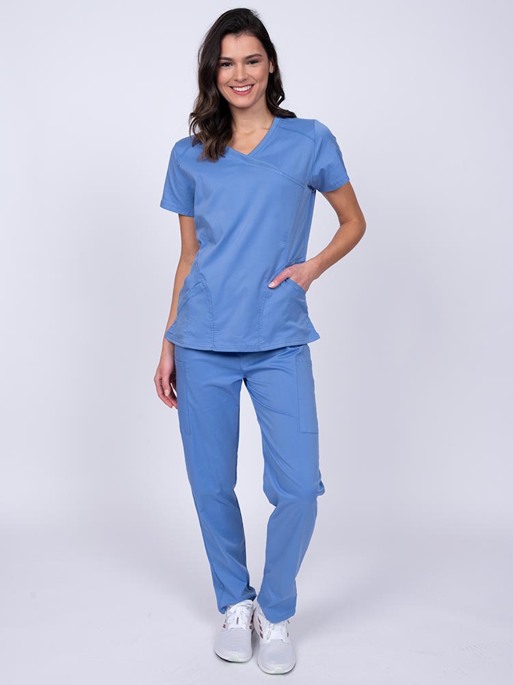 Young female healthcare worker wearing an Epic by MedWorks Women's Knit Collar Mock Wrap Scrub Top in ceil featuring a 2 way stretch fabric that allows air to pass easily through the garment.