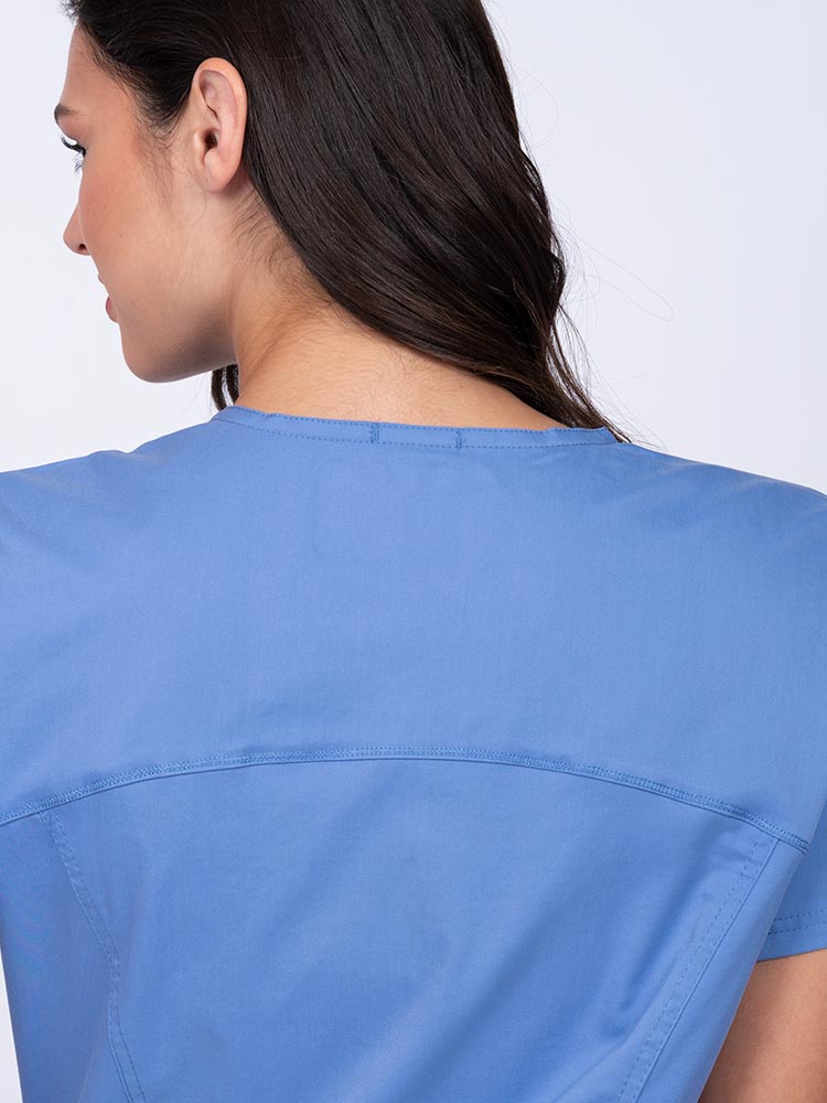 Young woman wearing an Epic by MedWorks Women's Knit Collar Mock Wrap Scrub Top in ceil with a back yoke to ensure a flattering fit.