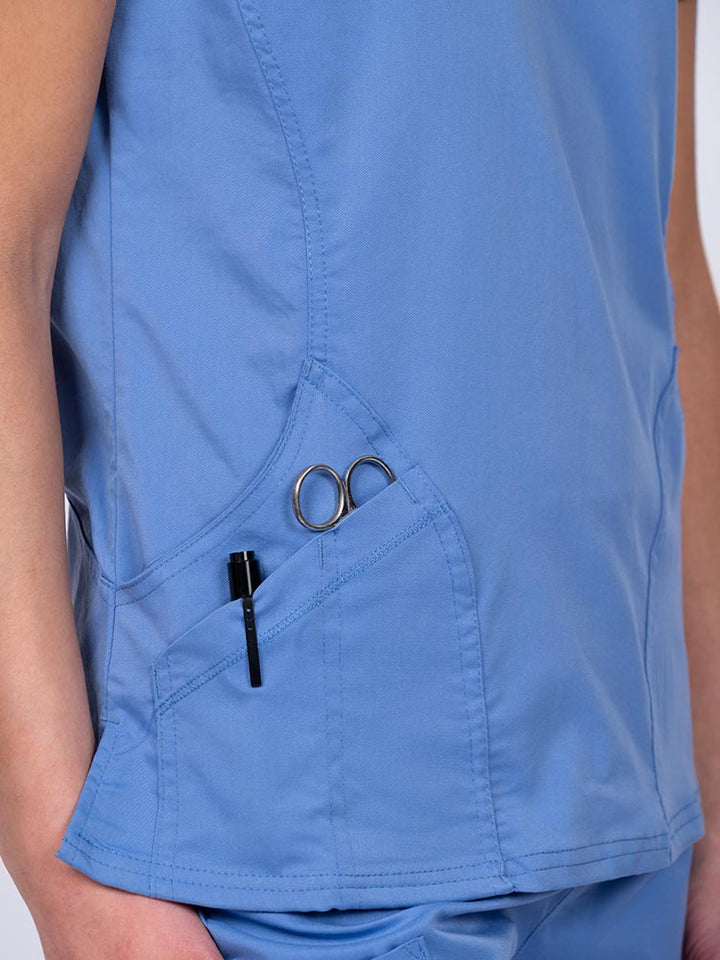 Woman wearing an Epic by MedWorks Women's Knit Collar Mock Wrap Scrub Top in ceil with two outside utility pockets on the wearer's right side.