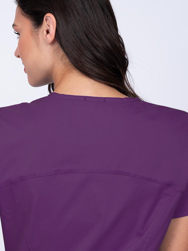 Young woman wearing an Epic by MedWorks Women's Knit Collar Mock Wrap Scrub Top in eggplant with a back yoke to ensure a flattering fit.