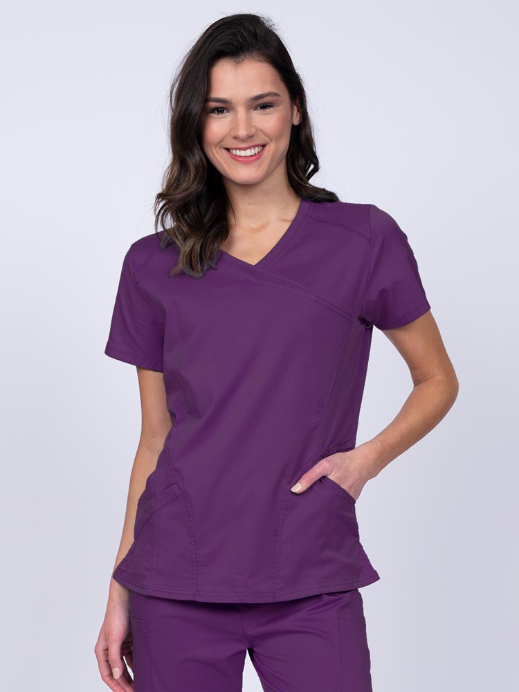 Young RN wearing an Epic by MedWorks Women's Knit Collar Mock Wrap Scrub Top in eggplant featuring a Y-neckline with short sleeves.