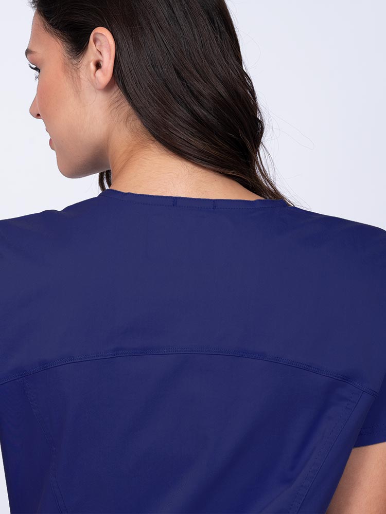 Young woman wearing an Epic by MedWorks Women's Knit Collar Mock Wrap Scrub Top in navy with a back yoke to ensure a flattering fit.
