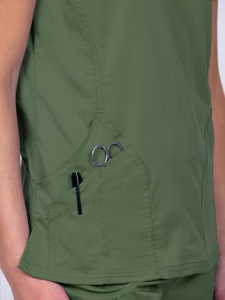 Woman wearing an Epic by MedWorks Women's Knit Collar Mock Wrap Scrub Top in olive with two outside utility pockets on the wearer's right side.