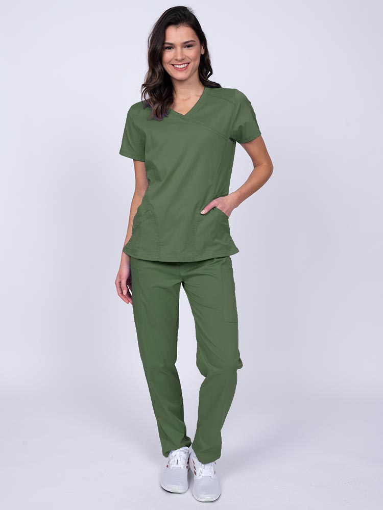 Young female healthcare worker wearing an Epic by MedWorks Women's Knit Collar Mock Wrap Scrub Top in olive featuring a 2 way stretch fabric that allows air to pass easily through the garment.