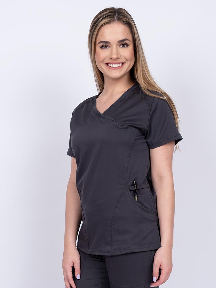 Young RN wearing an Epic by MedWorks Women's Knit Collar Mock Wrap Scrub Top in pewter featuring a Y-neckline with short sleeves.