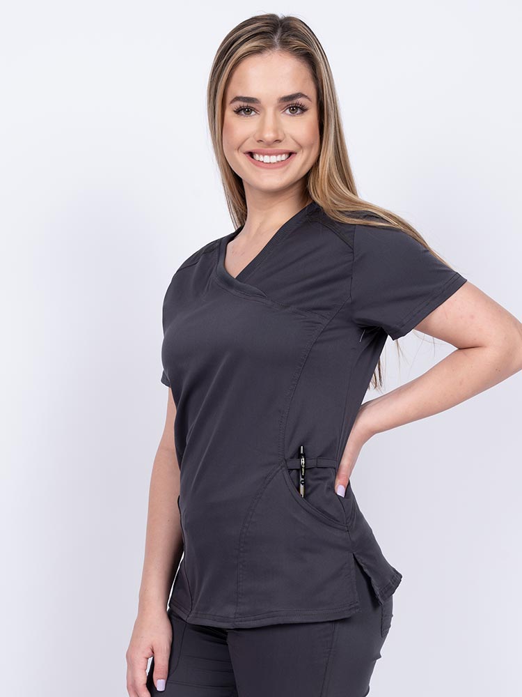 Woman wearing an Epic by MedWorks Women's Knit Collar Mock Wrap Scrub Top in pewter featuring two front slash pockets. 