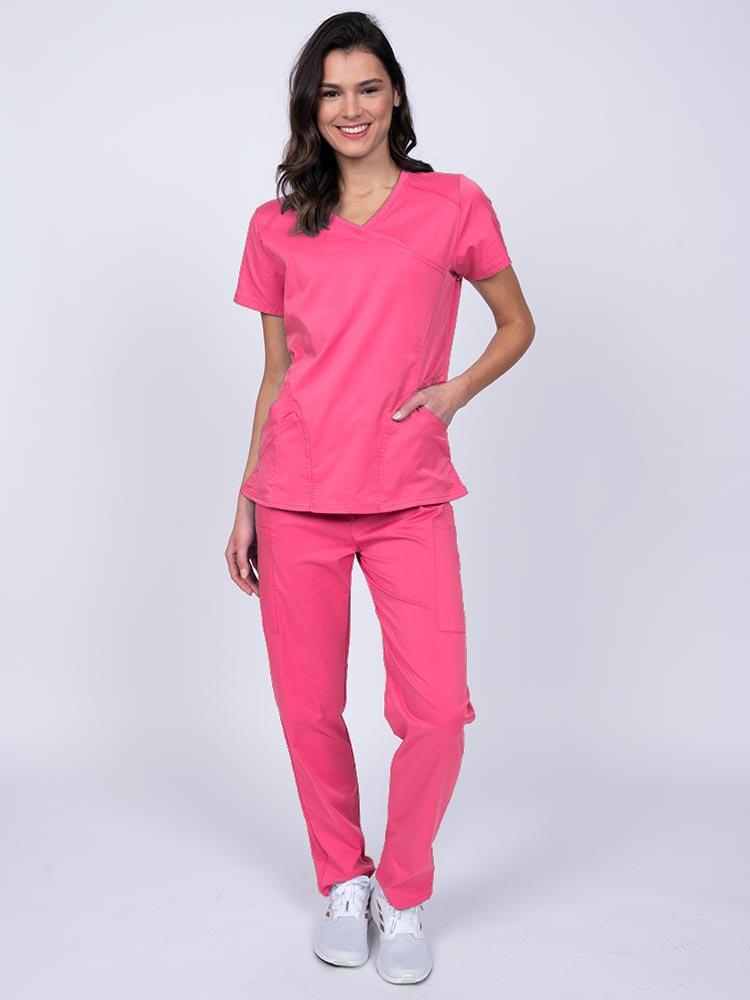 Young female healthcare worker wearing an Epic by MedWorks Women's Knit Collar Mock Wrap Scrub Top in shocking pink featuring a 2 way stretch fabric that allows air to pass easily through the garment.