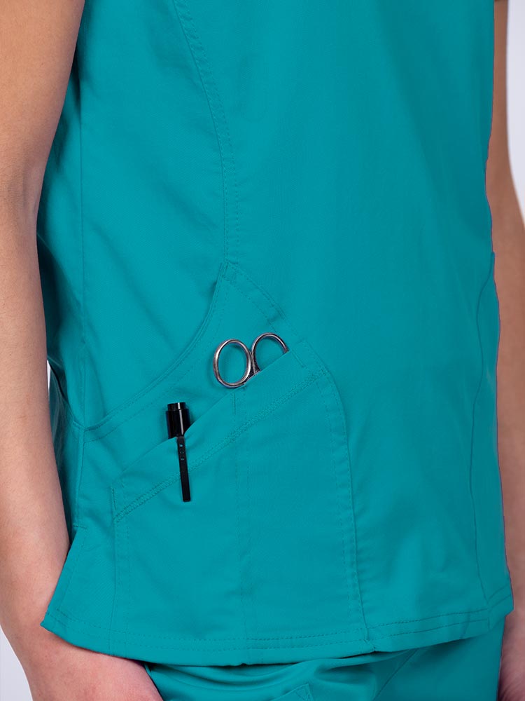 Woman wearing an Epic by MedWorks Women's Knit Collar Mock Wrap Scrub Top in teal with two outside utility pockets on the wearer's right side.
