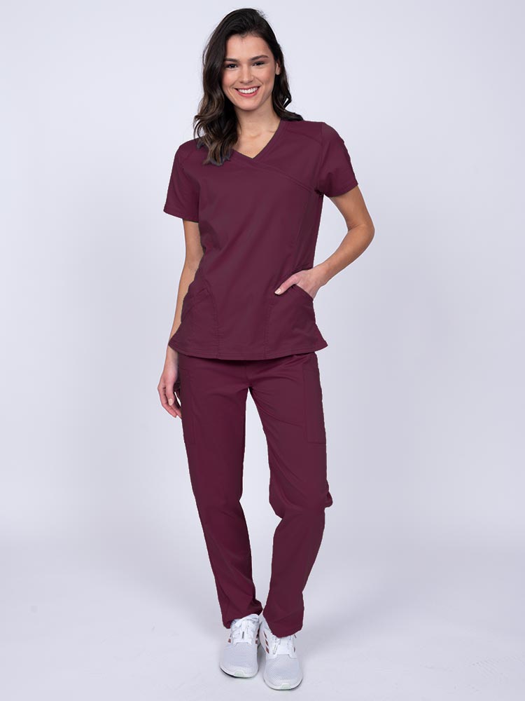 Young female healthcare worker wearing an Epic by MedWorks Women's Knit Collar Mock Wrap Scrub Top in wine featuring a 2 way stretch fabric that allows air to pass easily through the garment.