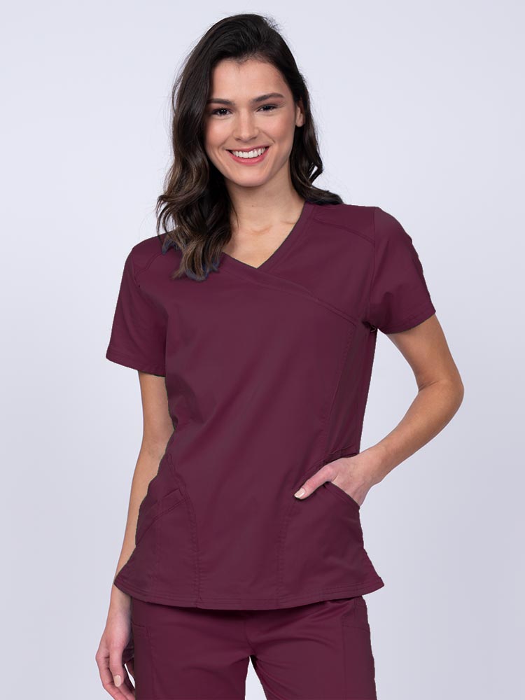 Young RN wearing an Epic by MedWorks Women's Knit Collar Mock Wrap Scrub Top in wine featuring a Y-neckline with short sleeves.