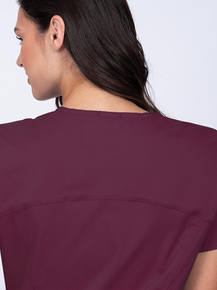 Young woman wearing an Epic by MedWorks Women's Knit Collar Mock Wrap Scrub Top in wine with a back yoke to ensure a flattering fit.
