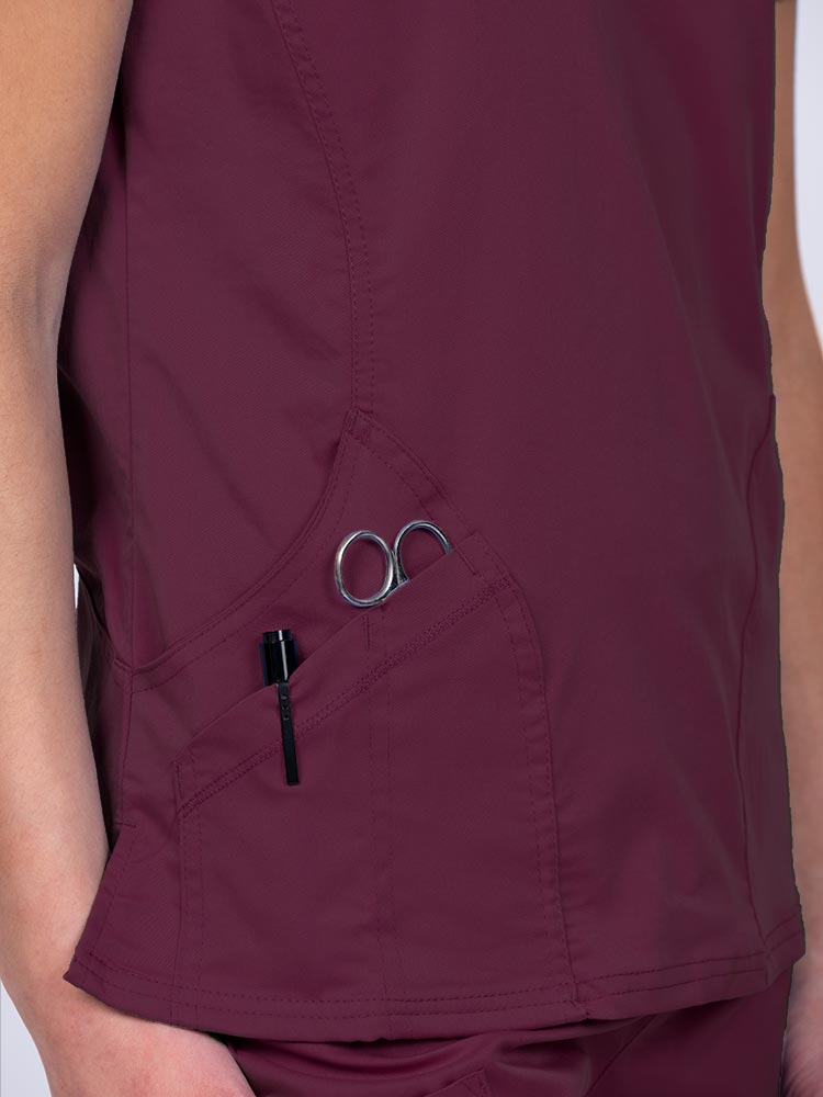Woman wearing an Epic by MedWorks Women's Knit Collar Mock Wrap Scrub Top in wine with two outside utility pockets on the wearer's right side.