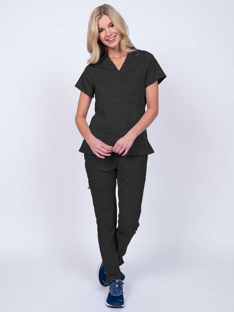 A young female healthcare worker wearing an Epic by MedWorks Women's Mock Wrap Scrub Top in black featuring a super soft, 2-way stretch fabric.