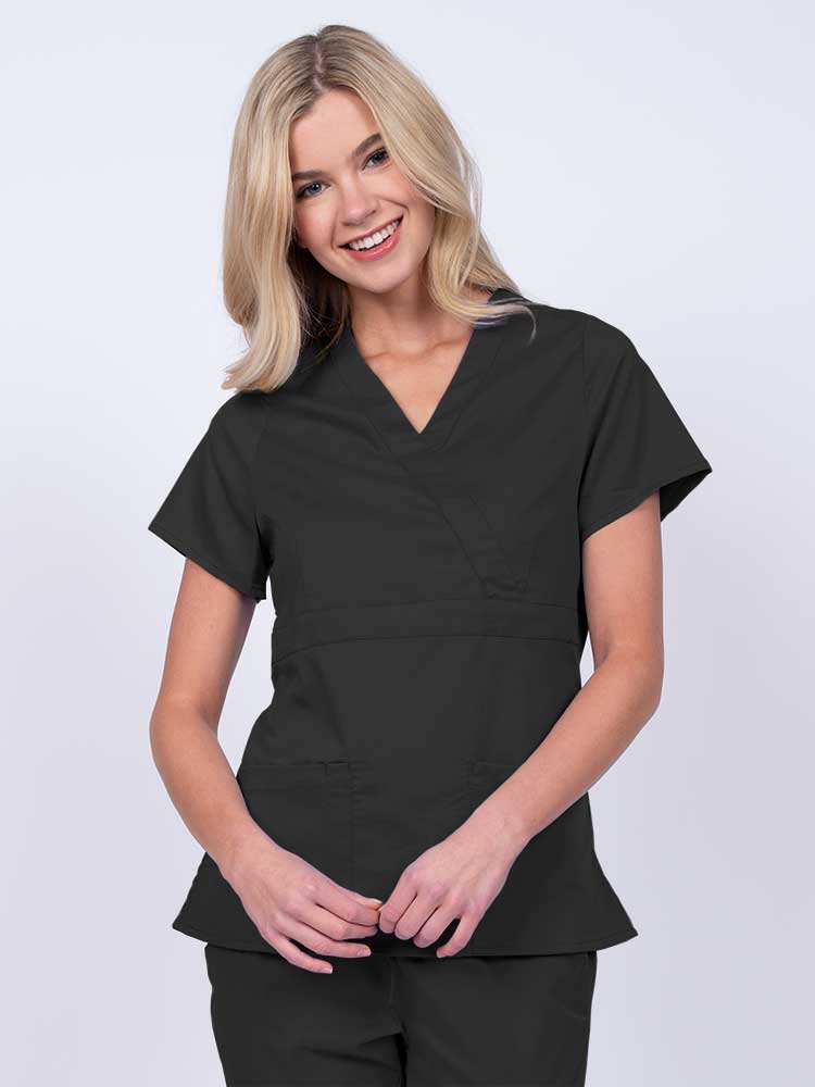 Young woman wearing an Epic by MedWorks Women's Mock Wrap Scrub Top in black with a unique fabric content of 77% Polyester, 21% Viscose, 2% Spandex.