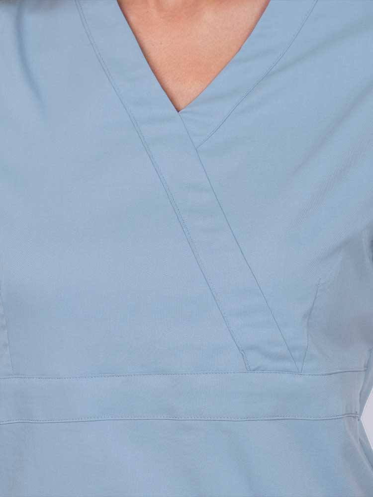 Young woman wearing an Epic by MedWorks Women's Mock Wrap Scrub Top in blue fog featuring a mock wrap neckline and stylish front seaming.