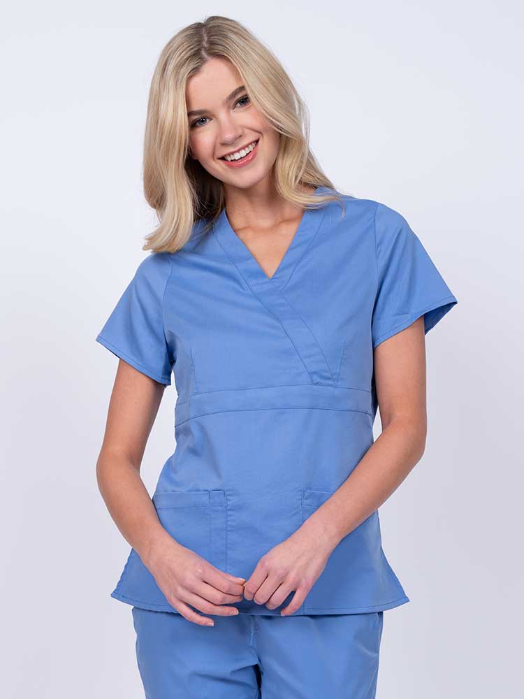 Young woman wearing an Epic by MedWorks Women's Mock Wrap Scrub Top in ceil with a unique fabric content of 77% Polyester, 21% Viscose, 2% Spandex.