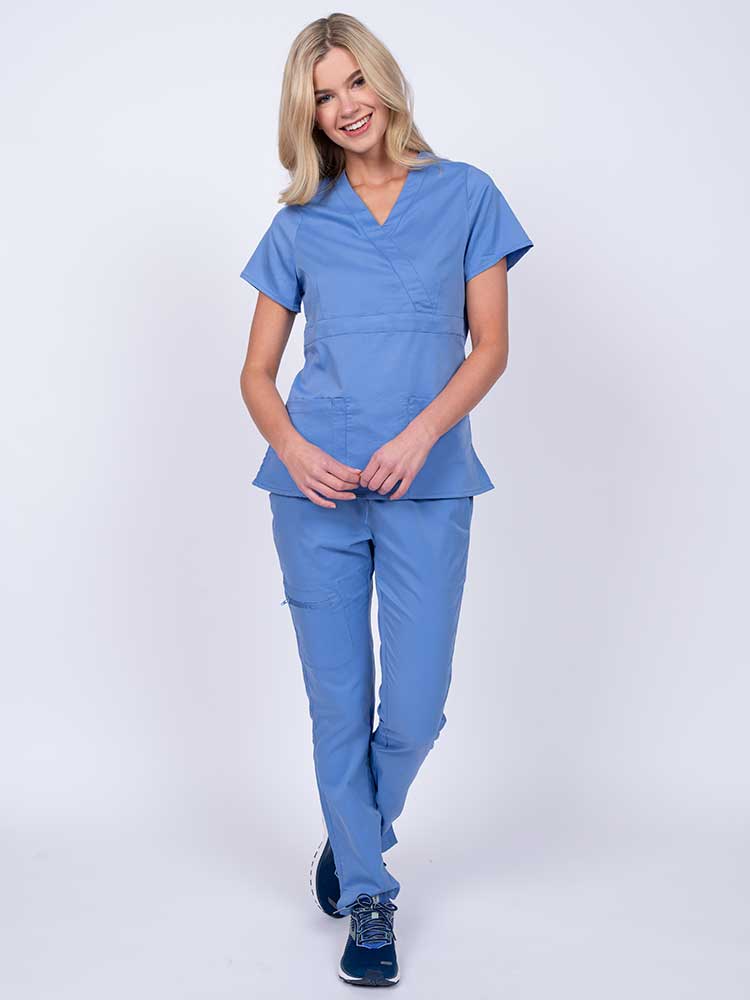 A young female healthcare worker wearing an Epic by MedWorks Women's Mock Wrap Scrub Top in ceil featuring a super soft, 2-way stretch fabric.