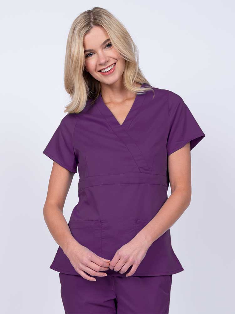 Young woman wearing an Epic by MedWorks Women's Mock Wrap Scrub Top in eggplant with a unique fabric content of 77% Polyester, 21% Viscose, 2% Spandex.