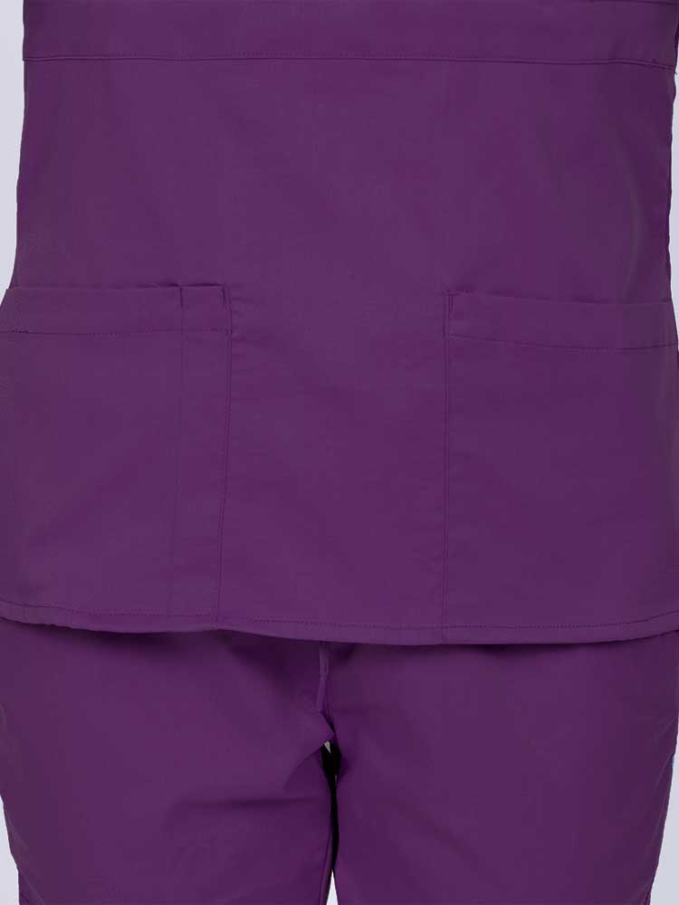 Woman wearing an Epic by MedWorks Women's Mock Wrap Scrub Top in eggplant featuring two front patch pockets.