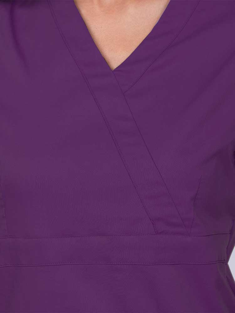 Young woman wearing an Epic by MedWorks Women's Mock Wrap Scrub Top in eggplant featuring a mock wrap neckline and stylish front seaming.