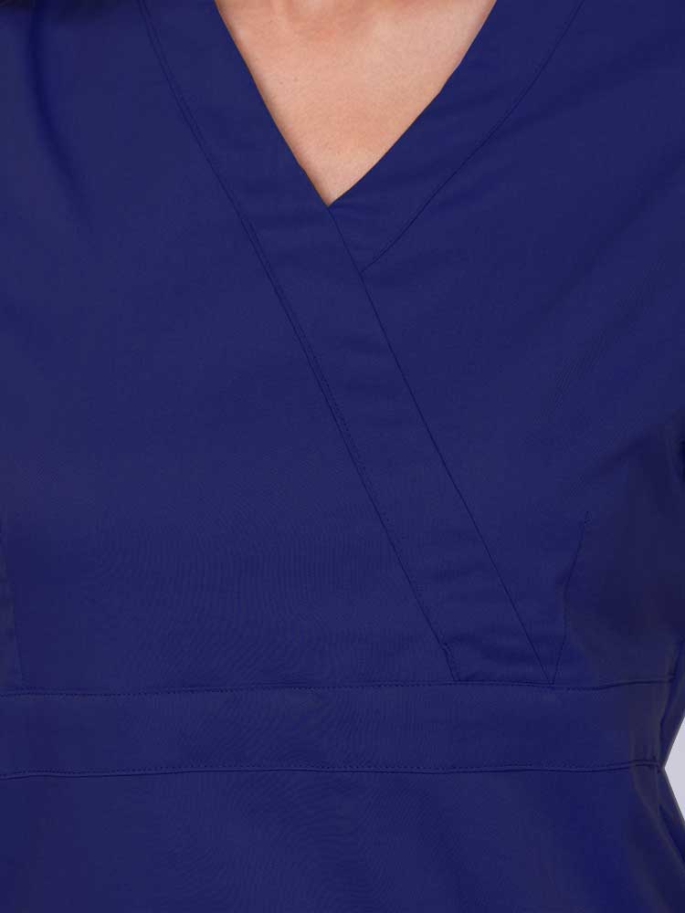 Young woman wearing an Epic by MedWorks Women's Mock Wrap Scrub Top in navy featuring a mock wrap neckline and stylish front seaming.