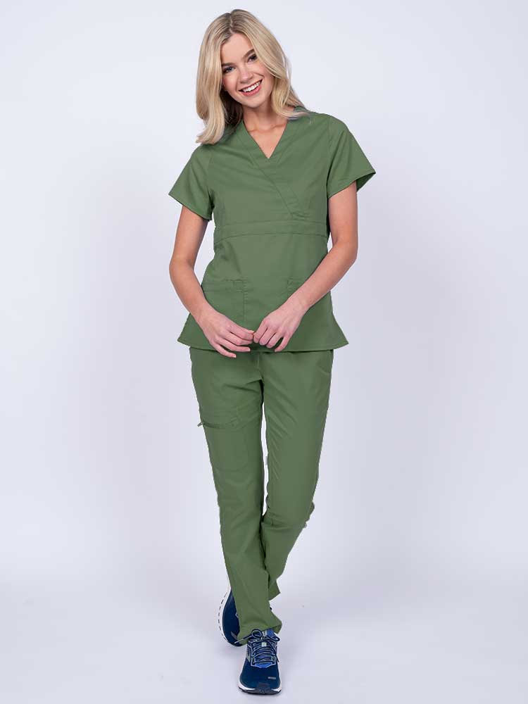 A young female healthcare worker wearing an Epic by MedWorks Women's Mock Wrap Scrub Top in olive featuring a super soft, 2-way stretch fabric.