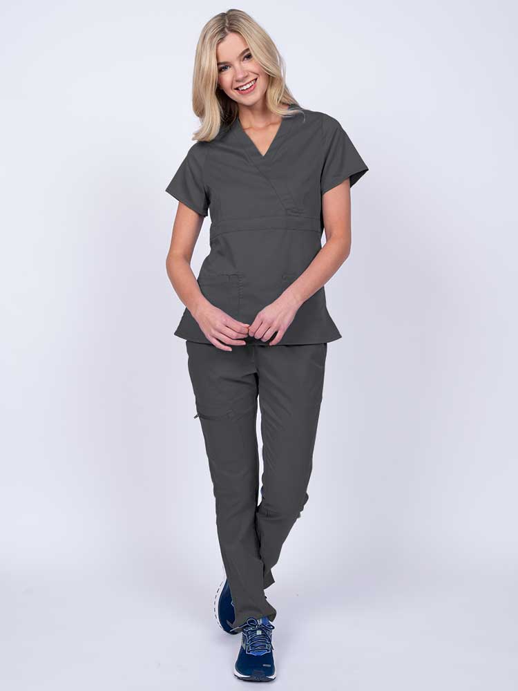 A young female healthcare worker wearing an Epic by MedWorks Women's Mock Wrap Scrub Top in pewter featuring a super soft, 2-way stretch fabric.