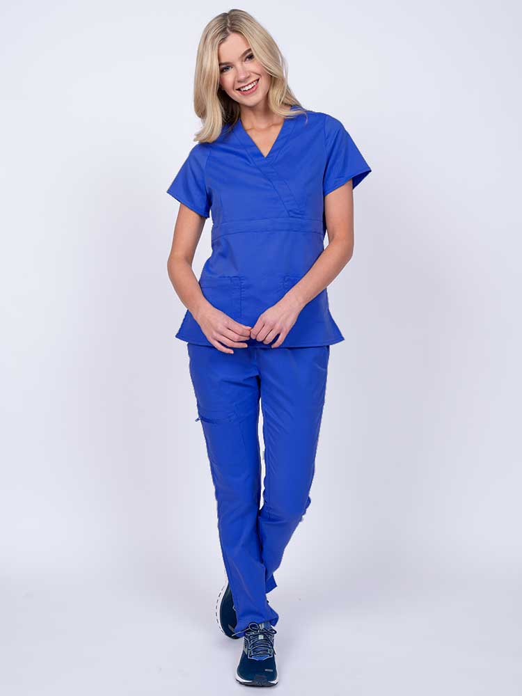 A young female healthcare worker wearing an Epic by MedWorks Women's Mock Wrap Scrub Top in royal featuring a super soft, 2-way stretch fabric.