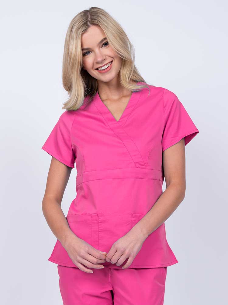 Young woman wearing an Epic by MedWorks Women's Mock Wrap Scrub Top in shocking pink with a unique fabric content of 77% Polyester, 21% Viscose, 2% Spandex.