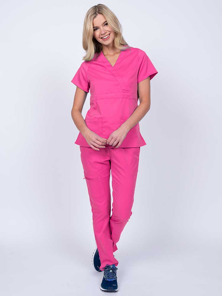 A young female healthcare worker wearing an Epic by MedWorks Women's Mock Wrap Scrub Top in shocking pink featuring a super soft, 2-way stretch fabric.