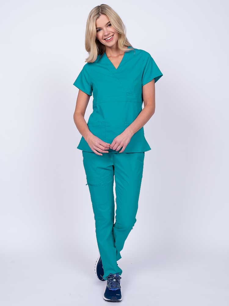 A young female healthcare worker wearing an Epic by MedWorks Women's Mock Wrap Scrub Top in teal featuring a super soft, 2-way stretch fabric.