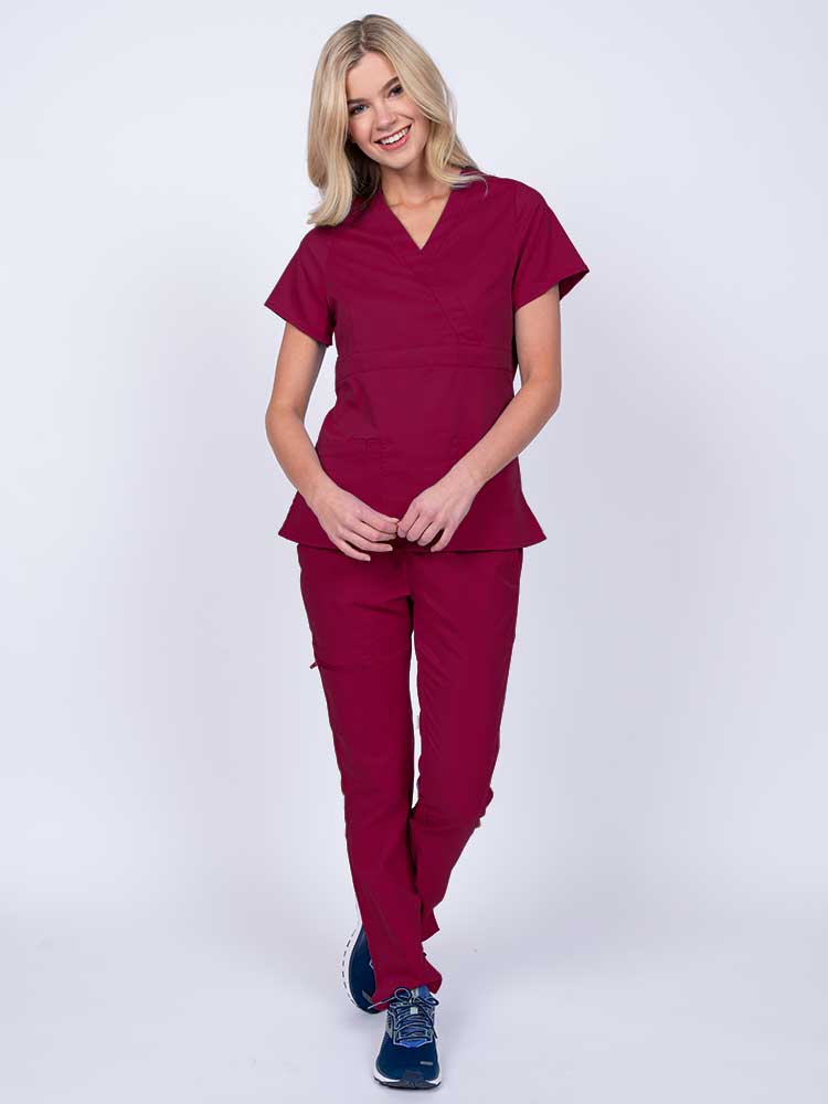 A young female healthcare worker wearing an Epic by MedWorks Women's Mock Wrap Scrub Top in wine featuring a super soft, 2-way stretch fabric.
