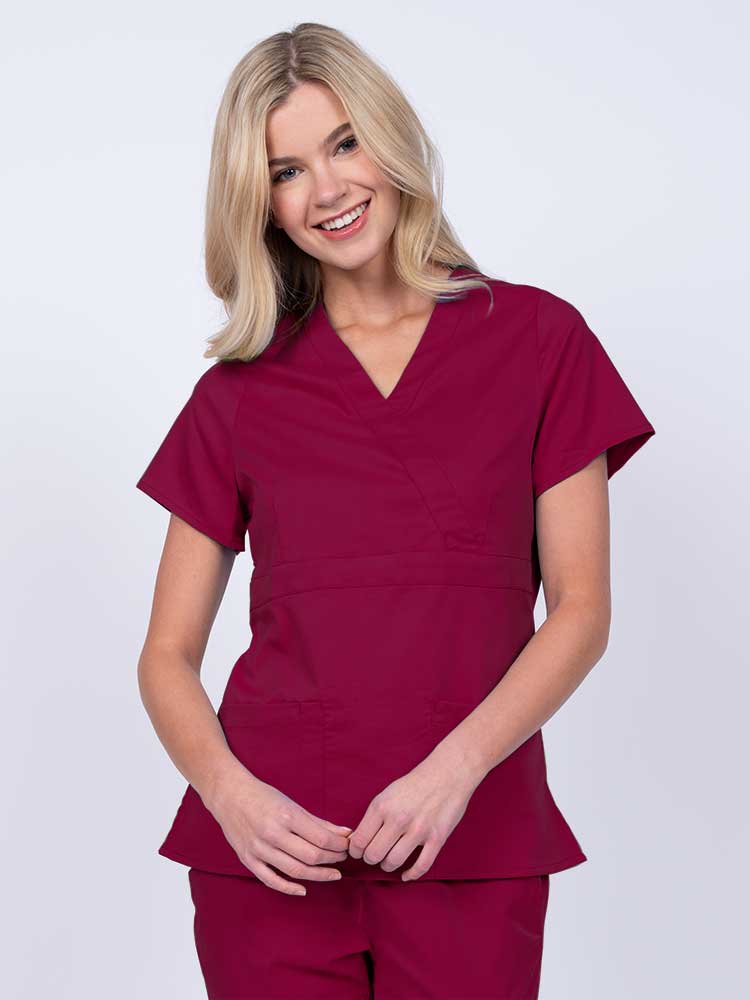 Young woman wearing an Epic by MedWorks Women's Mock Wrap Scrub Top in wine with a unique fabric content of 77% Polyester, 21% Viscose, 2% Spandex.
