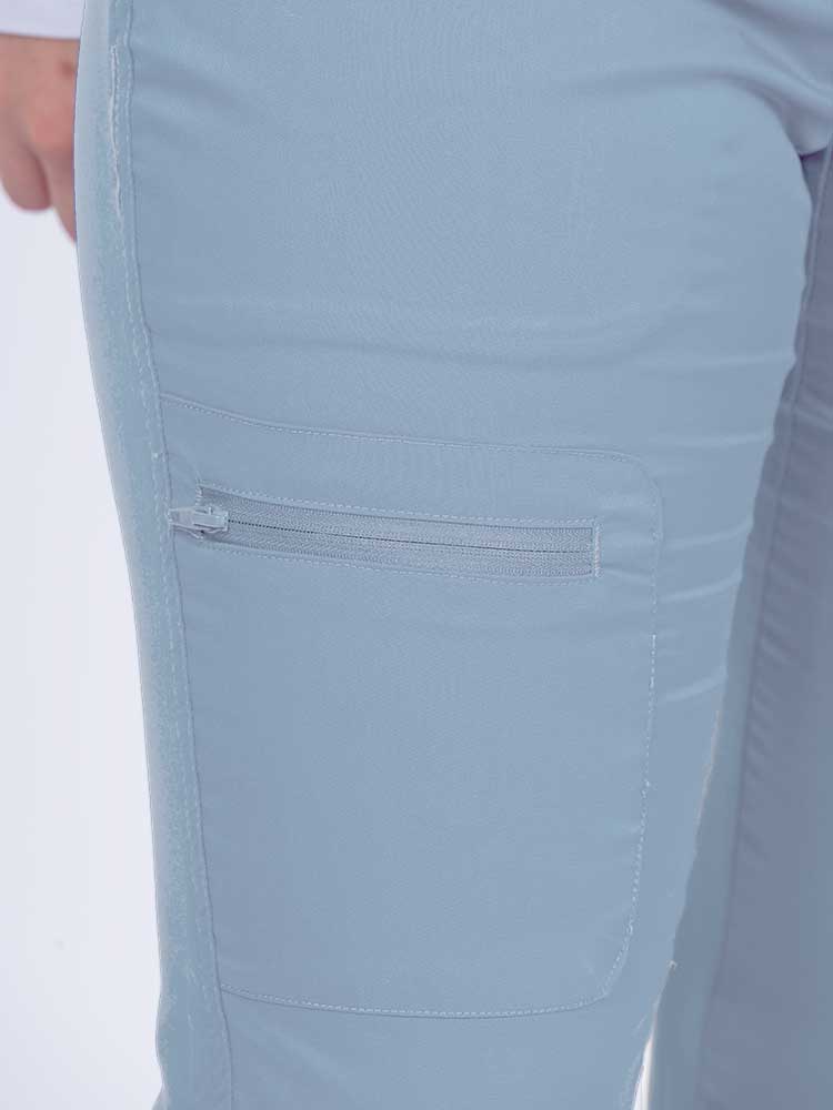 Young female nurse wearing an Epic by MedWorks Women's Blessed Skinny Yoga Scrub Pant in blue fog with 1 zip closure cargo pant on the wearer's right.