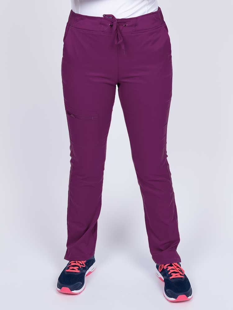 Young healthcare worker wearing an Epic by MedWorks Women's Blessed Skinny Yoga Scrub Pant in eggplant featuring side slits for additional range of motion.