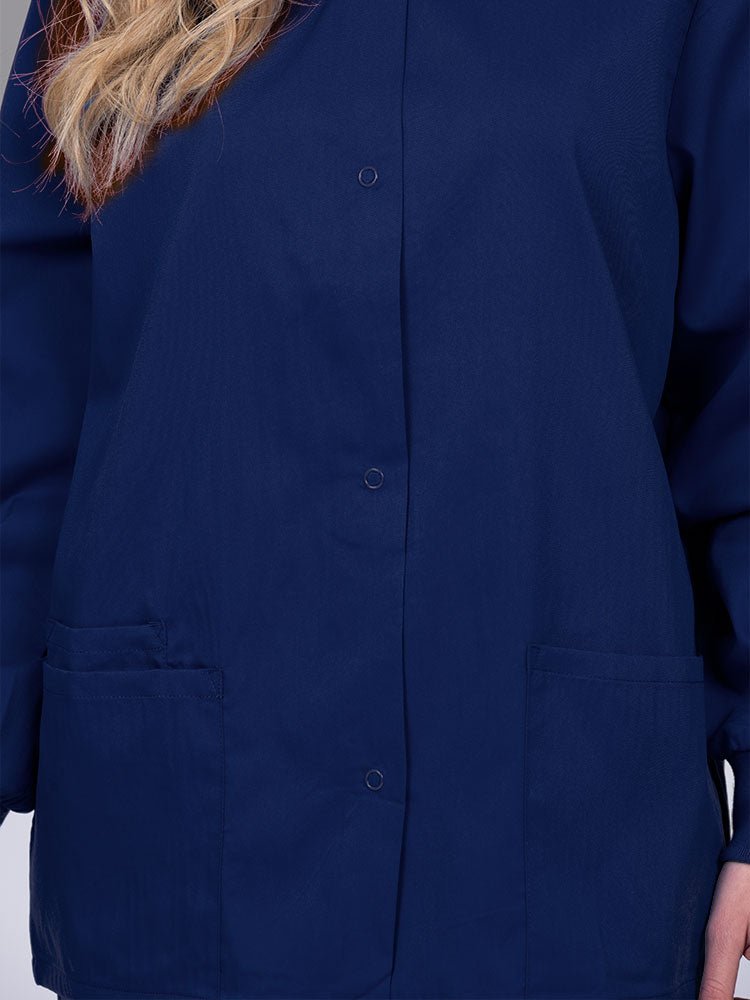 Young nurse wearing an Epic by MedWorks Women's Snap Front Scrub Jacket in navy with color matched metal snap closure.