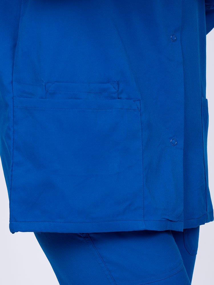 Young healthcare professional wearing an Epic by MedWorks Women's Snap Front Scrub Jacket in royal with 1 interior cell phone pocket on wearer's right side.