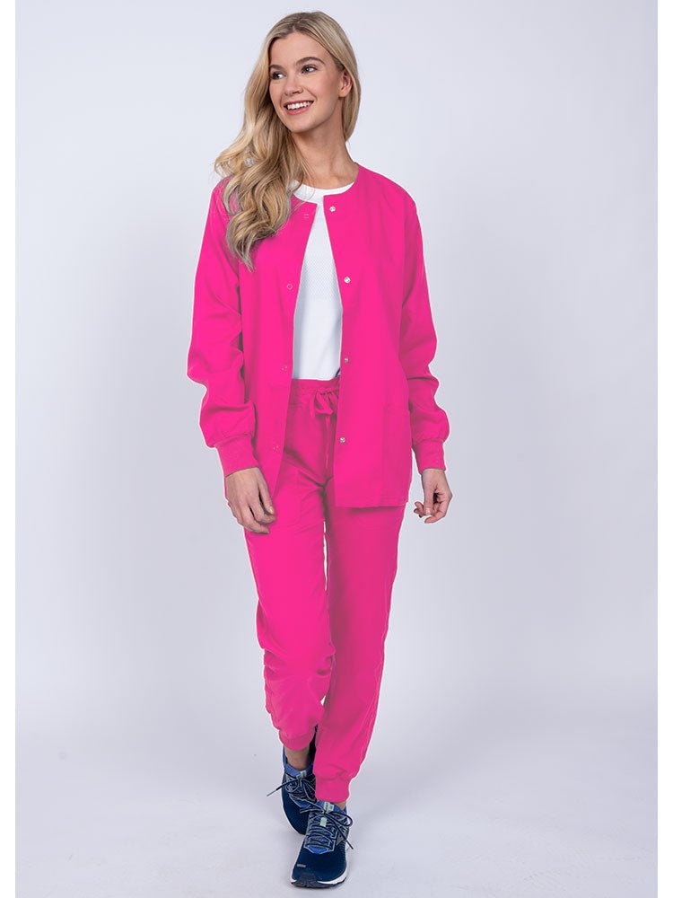 Woman wearing an Epic by MedWorks Women's Snap Front Scrub Jacket in shocking pink with rib knit cuffs.