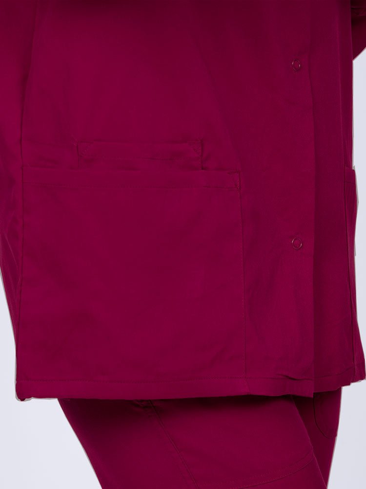 Young healthcare professional wearing an Epic by MedWorks Women's Snap Front Scrub Jacket in wine with 1 interior cell phone pocket on wearer's right side.