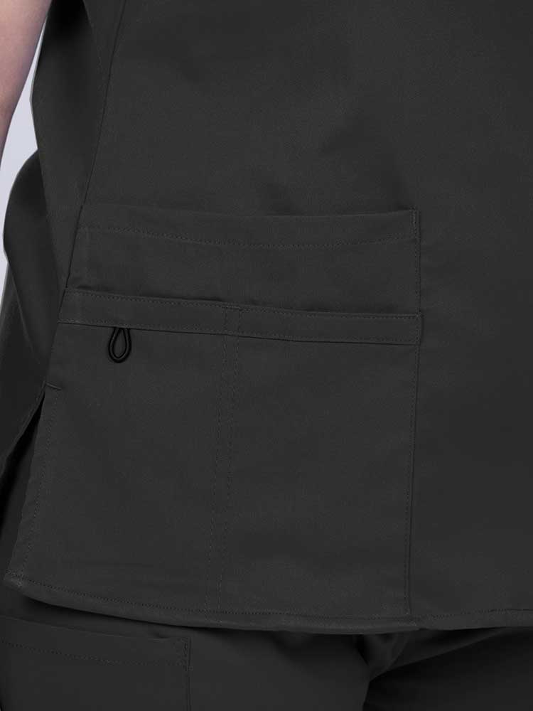 Young female healthcare worker wearing an Epic by MedWorks Women's Y-Neck Scrub Top in black with 1 double outer pocket on the wearer's right side.