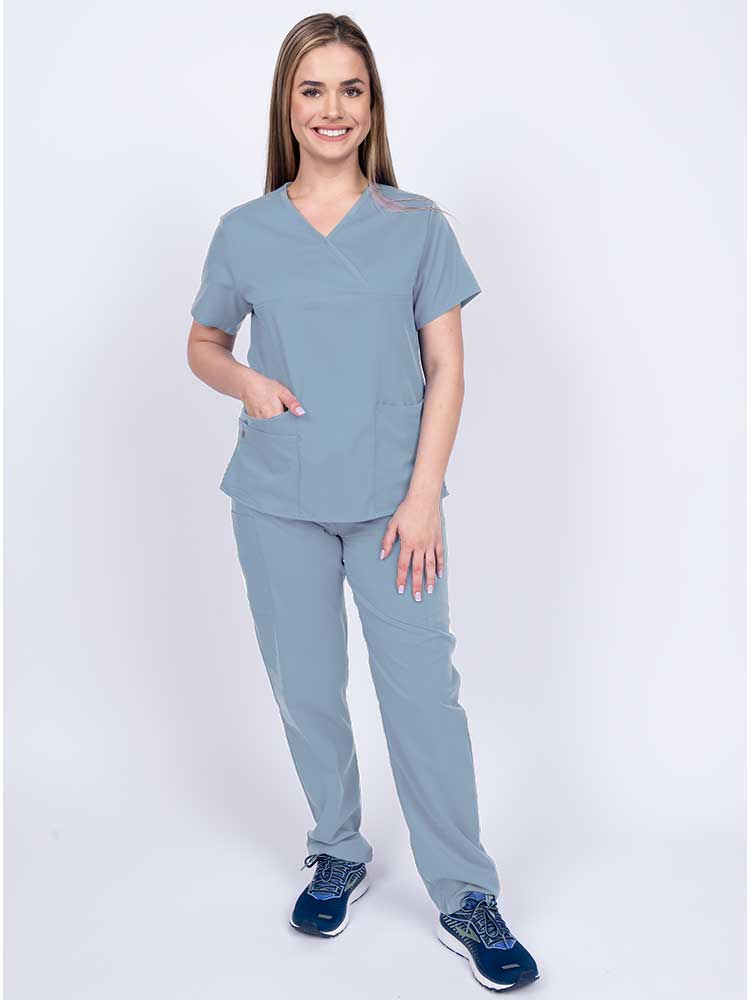 Young woman wearing an Epic by MedWorks Women's Y-Neck Scrub Top in blue fog with 2 front patch pockets.