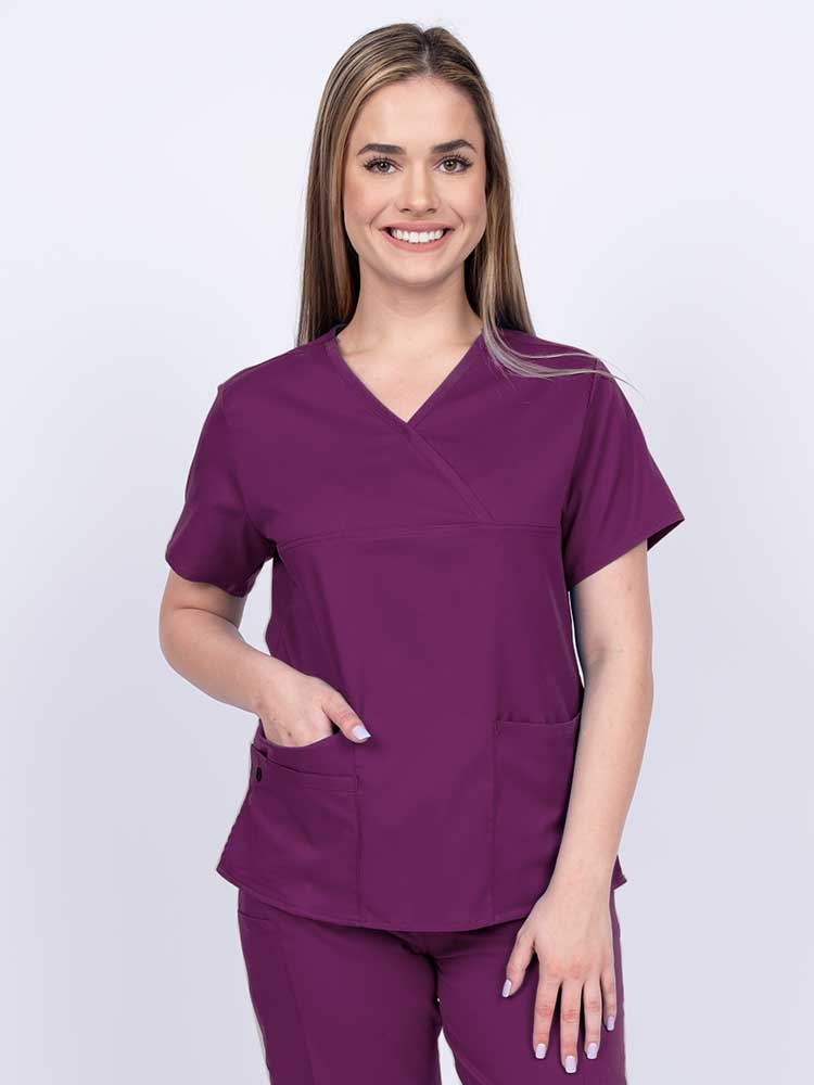 Young woman wearing an Epic by MedWorks Women's Y-Neck Scrub Top in eggplant with 2 front patch pockets.