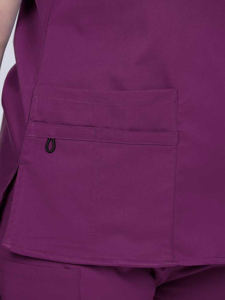 Young female healthcare worker wearing an Epic by MedWorks Women's Y-Neck Scrub Top in eggplant with 1 double outer pocket on the wearer's right side.