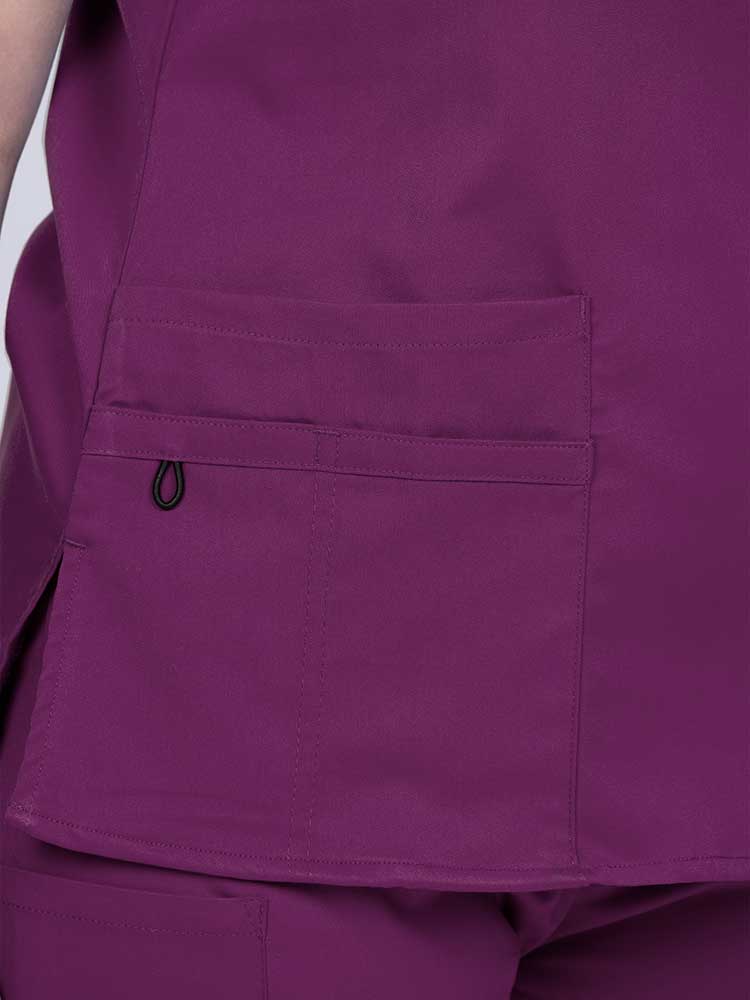 Young female healthcare worker wearing an Epic by MedWorks Women's Y-Neck Scrub Top in eggplant with 1 double outer pocket on the wearer's right side.