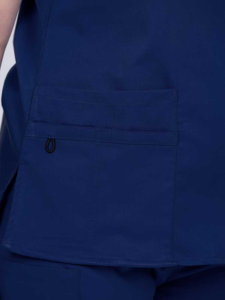 Young female healthcare worker wearing an Epic by MedWorks Women's Y-Neck Scrub Top in navy with 1 double outer pocket on the wearer's right side.