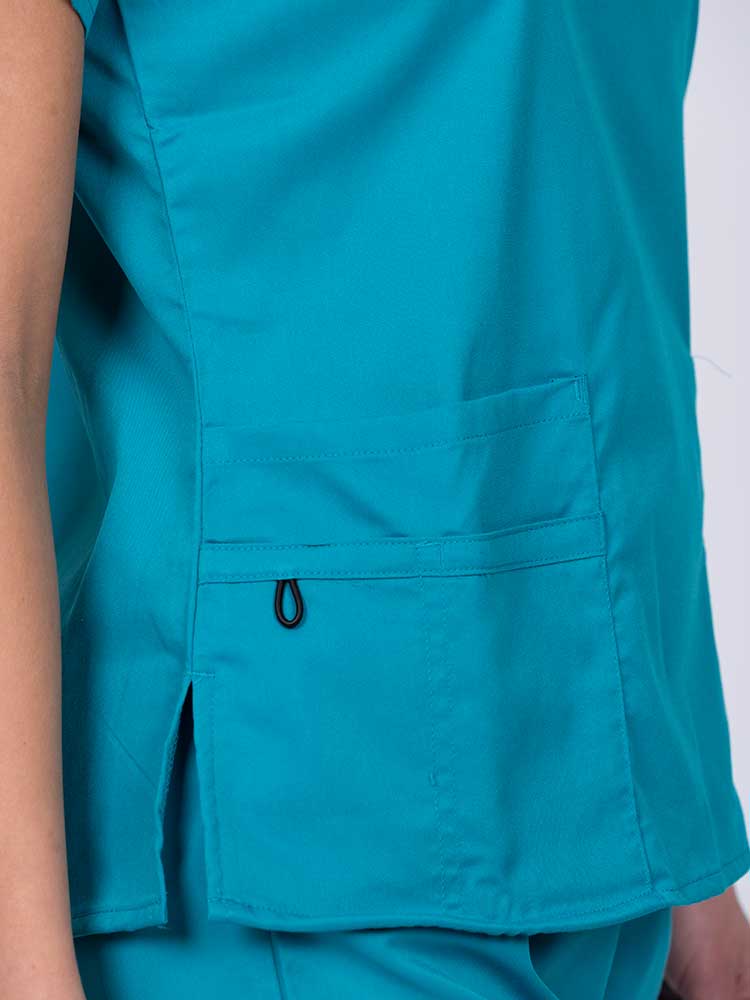 Young female healthcare worker wearing an Epic by MedWorks Women's Y-Neck Scrub Top in teal with 1 double outer pocket on the wearer's right side.