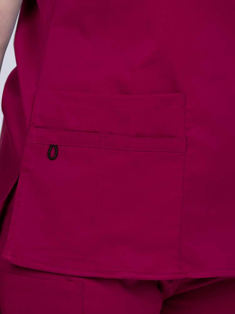 Young female healthcare worker wearing an Epic by MedWorks Women's Y-Neck Scrub Top in wine with 1 double outer pocket on the wearer's right side.