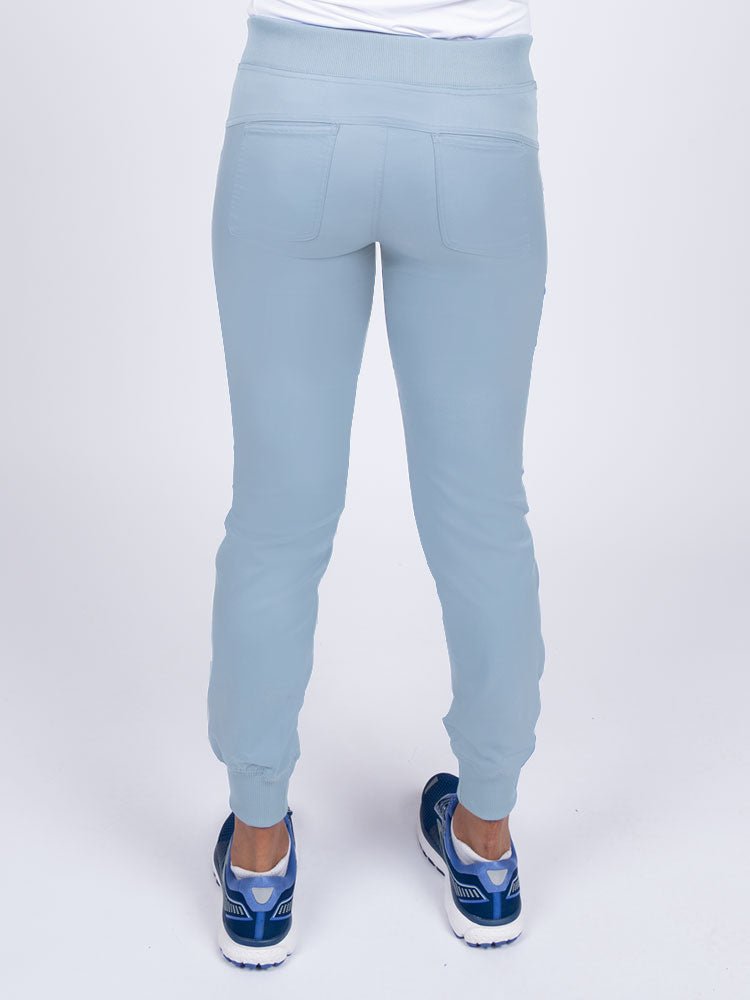 A young female Nurse Practitioner wearing an Epic by MedWorks Women's Yoga Jogger Scrub Pant in Blue Fog size small featuring 2 back patch pockets.